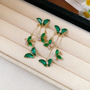 Elegant gold butterfly tassel earrings with green gemstones on a beige velvet jewelry box