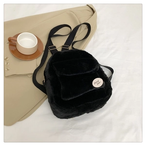 Mini mochila de felpa negra con etiqueta good luck mostrada en un entorno de estilo