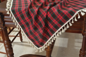 Detail of red and green Christmas plaid tablecloth with fringe on a vintage wooden table