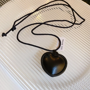 Detail view of a black 3D heart pendant with vintage rope texture on a woven cord