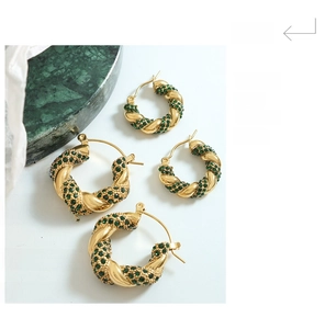 Detailed macro view of U-shaped twisted gold earrings with micro-set green zircons