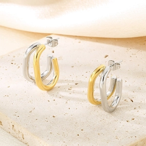 Détail macro de boucles d'oreilles en U bicolores or et argent sur socle beige