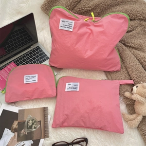 Three-piece pink nylon travel storage bags with neon zippers on a soft white rug