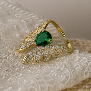 Macro detail of gold wing ring with green pear-cut zircon on elegant lace background