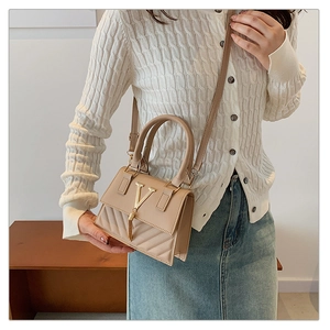 Detail of beige quilted small crossbody bag with V-shaped metal buckle and tassel charm