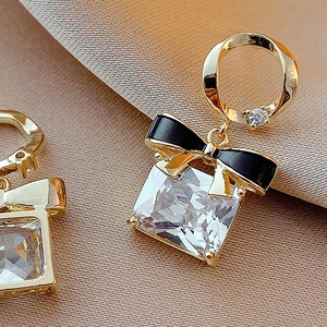 Boucles d'oreilles nœud dorées avec émail noir et zircon carré sur satin luxueux