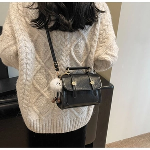 Detail of black vintage crossbody bag with a white plush monster charm on a beige sweater
