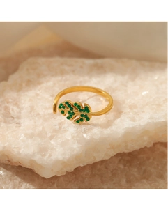 Macro detail of leaf-shaped gold ring with inlaid green crystals on white crystal stone