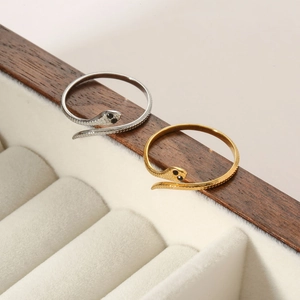 Detail of gold and silver snake rings with scale texture and black stones on a jewelry box