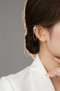 Close-up of golden double-loop chain ear cuff with sparkling zircons on female ear