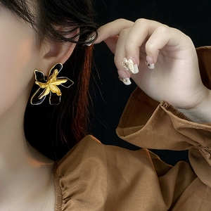 Close-up of model wearing black and gold double-layered flower stud earrings on black backdrop