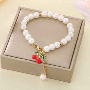 Detail of a pearl bracelet featuring a cherry pendant and gold clasp on a display stand