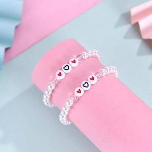 Détail de bracelets en perles avec cœur sur support rose, cadeau idéal pour la rentrée