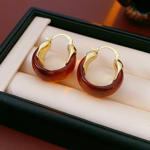 Detail of Au750 gold-plated earrings with translucent amber resin on a jewelry cushion