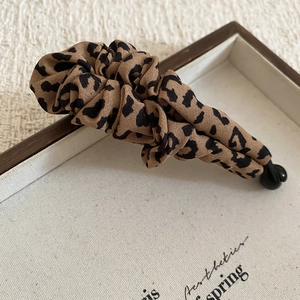 Close-up of leopard print fabric hair clip with pleated design on a wooden tray