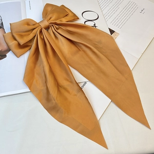 Detail of elegant caramel satin bow hair clip with long ribbons on a fashion magazine