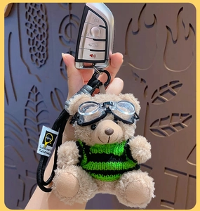 Close-up of cool teddy bear plush pendant in green striped sweater with goggles