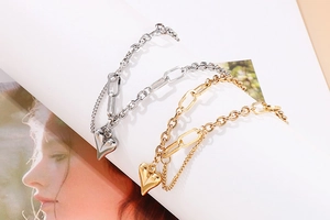 Detail of silver and gold heart pendant bracelets with paperclip chain on white background