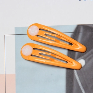 Close-up of two bright orange drip-paint BB hair clips with translucent round accents