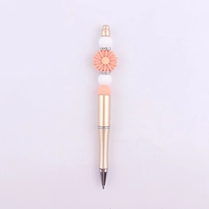 Close-up of golden beaded pen with pink daisy, white silicone beads, and rhinestone rings