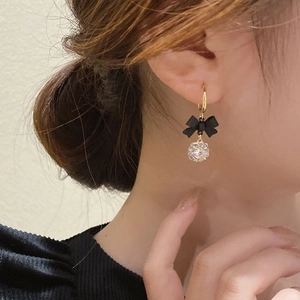 Macro detail of a gold hoop earring featuring a black bow and a zircon crystal bead on a model