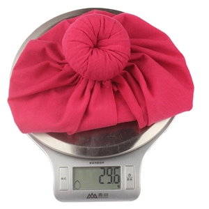Macro view of bright fuchsia soft knit baby donut hat on a digital scale weighing 29.6g