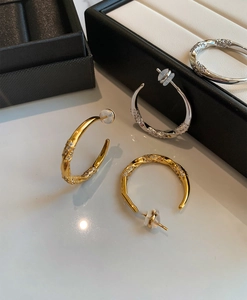 Detailed view of C-shaped gold and silver earrings with zircon stones on a white surface