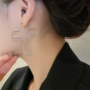 Gros plan d'un clou d'oreille croix argentée évidée porté avec un blazer sombre élégant