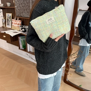 Detail of the green tweed makeup bag fabric and metal zipper held by a model