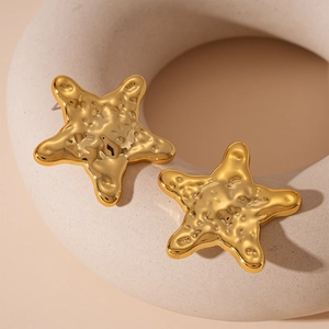 Macro shot of gold starfish earrings with textured hammered finish on white ceramic