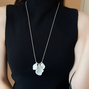 Close-up of three-petal pendant on a long silver chain worn over black garment