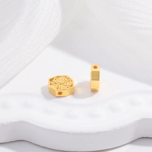 Detailed macro view of two gold hexagonal spacer beads with embossed floral patterns