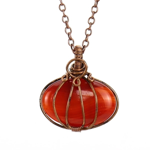 Macro view of handmade wire-wrapped carnelian stone pumpkin pendant with bronze metal detail