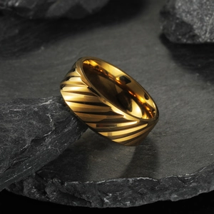 Men's gold titanium steel wedding band with textured diagonal grooves on dark rock