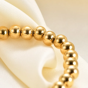 Polished 15mm stainless steel golden bead elastic bracelet on silk background