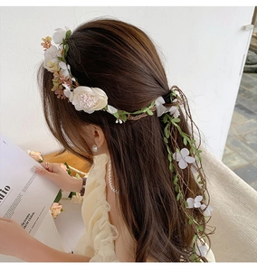 Detail of floral headpiece featuring white silk flowers, green leaves, and vine streamers
