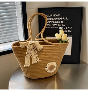Detail of khaki woven tote bag with lace bow and daisy embroidery on a metal table