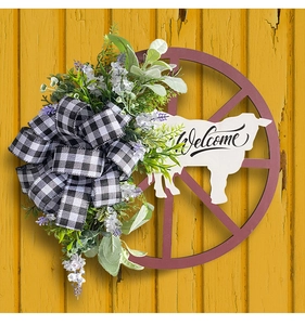 Close-up of rustic cow-themed welcome wreath with green foliage and buffalo plaid bow
