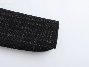 Detaillierte Makroansicht der schwarzen Tweed-Stofftextur und Manschette am Kleid