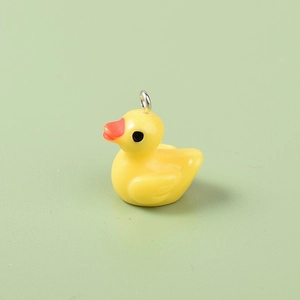 Detail view of a 3D yellow resin duck pendant with a silver metal loop on green surface