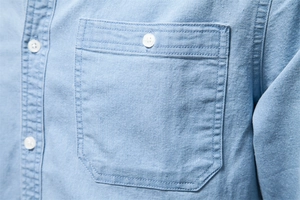 Detail of light blue denim shirt showing chest pocket, white buttons and premium stitching