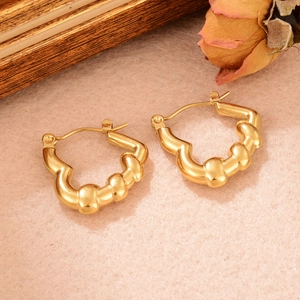 Gros plan de boucles d'oreilles dorées torsadées sur cadre bois et fleurs séchées