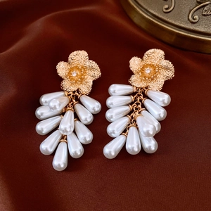 Close-up of golden wrinkled flower earrings with pearl tassels on silk fabric