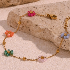 Detail of colorful beaded flower bracelet with gold chain on textured stone background