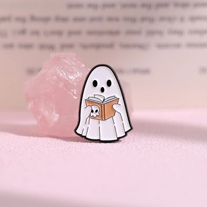 Macro shot of cute ghost enamel pin holding a skull book on a soft pink background