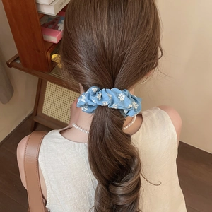 Close-up of a blue floral knit scrunchie with daisy pattern styled on a ponytail
