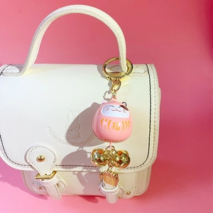 Pink Maneki Neko lucky cat keychain with golden bells on a beige handbag