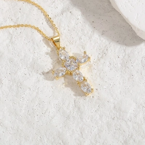Minimalist gold cross necklace with mixed-cut zircon stones on a white stone background