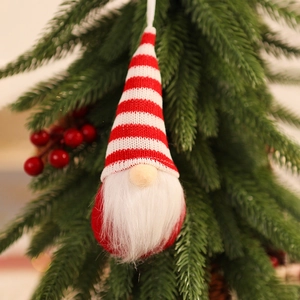 Detail of knitted Christmas gnome with red striped hat hanging on a festive tree branch