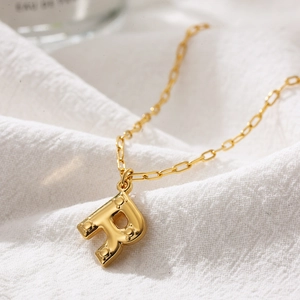 Macro shot of gold bubble initial R pendant with embossed dots on paperclip chain